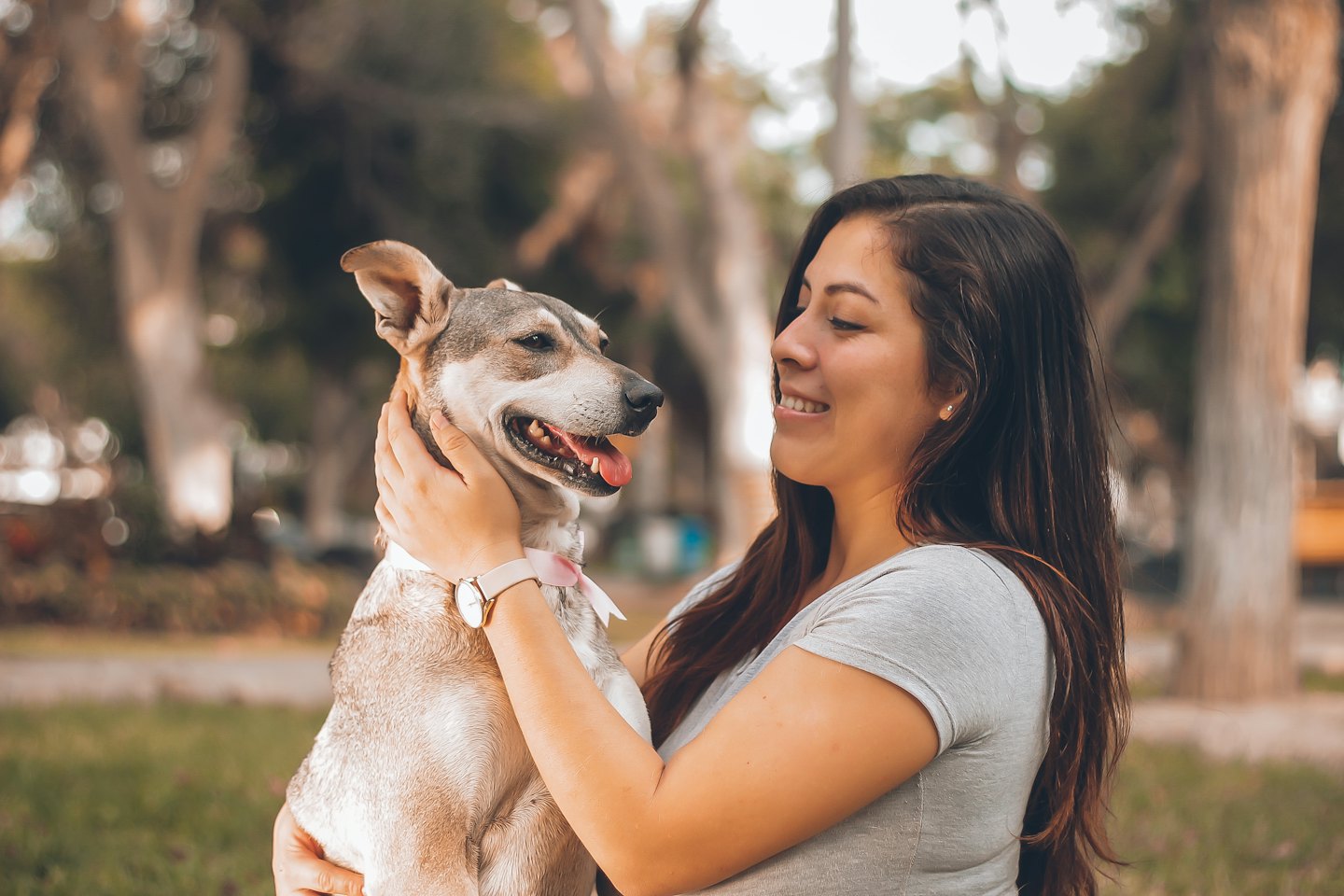 Woman smiling while holding a happy dog in a park.